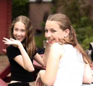 Zwei Mädchen lächeln und winken.